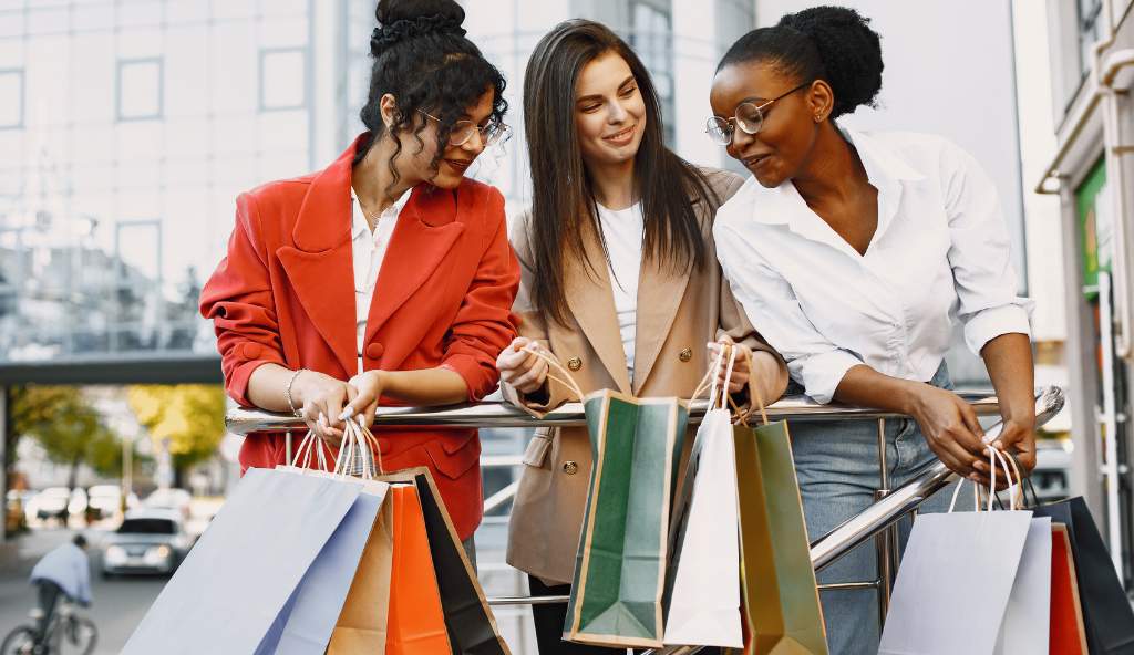 Three stylish women with shopping bags smiling and chatting outdoors in an urban setting products bundles