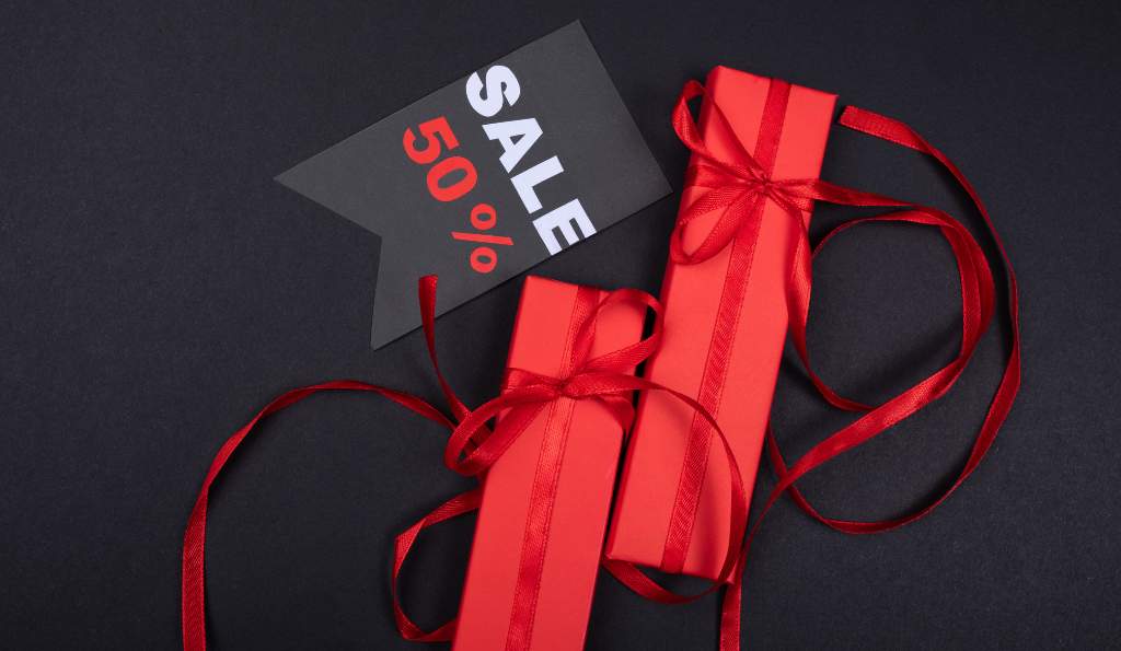 Black Friday sale concept with red gift boxes tied with ribbons and a black sale tag offering a 50% discount on a dark background season