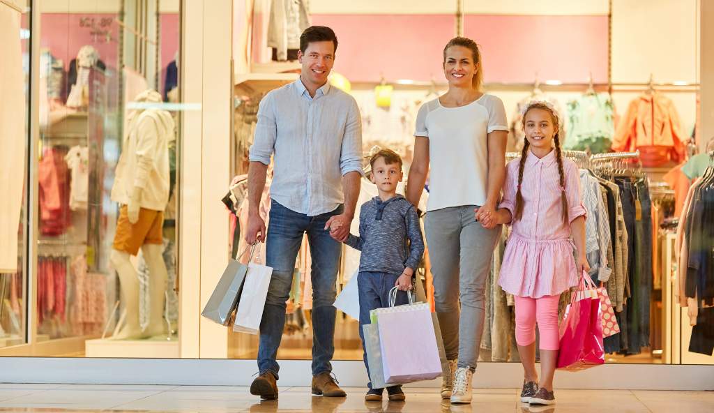 Happy family of four carrying shopping bags while walking out of a clothing store in a shopping mall bundles products