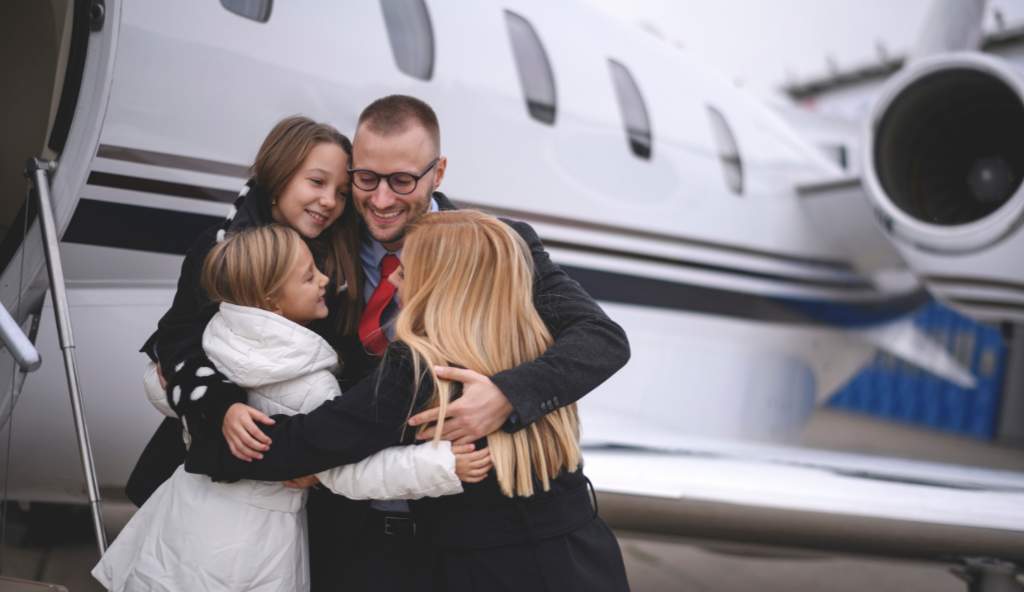 Happy family embracing a man in a suit near a private jet, showing a joyful reunion at the airport