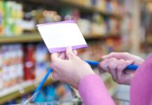 Product Bundles for Ultimate Savings Close-up of a person holding a shopping list while pushing a cart in a grocery store aisle, focusing on budgeting and planned shopping bundles