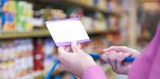 Product Bundles for Ultimate Savings Close-up of a person holding a shopping list while pushing a cart in a grocery store aisle, focusing on budgeting and planned shopping bundles