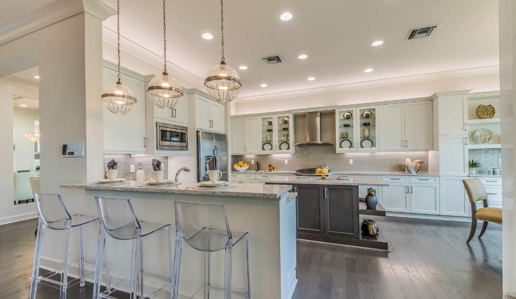 Elegant open-concept kitchen with white cabinetry, a large island, pendant lighting, glass barstools, stainless steel appliances, and decorative shelving, featuring a modern and sophisticated design furniture