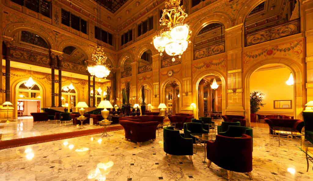 Luxurious hotel lobby with ornate golden architecture, marble flooring, grand chandeliers, and elegant seating arrangements