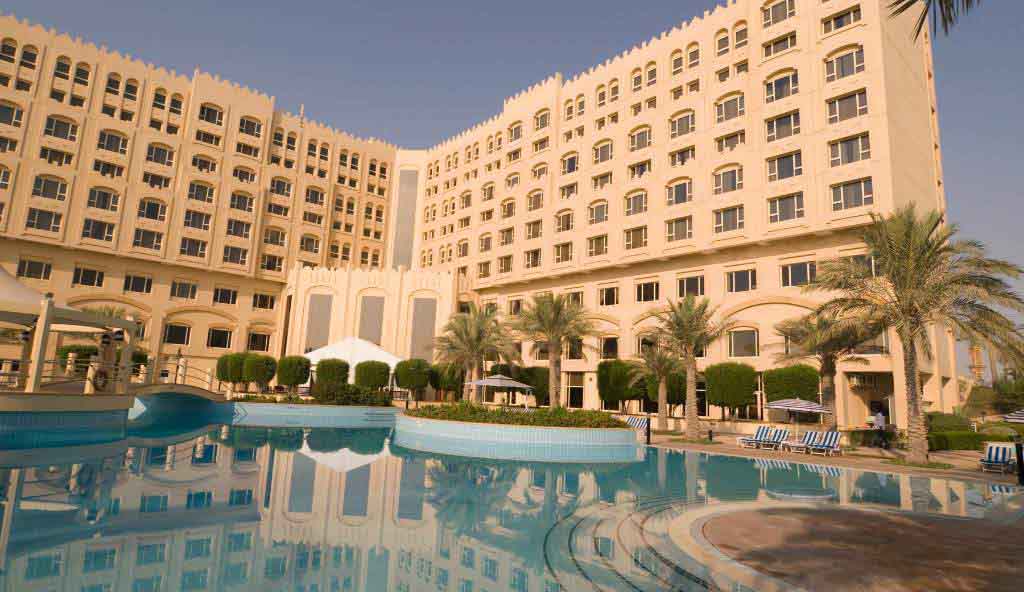 Luxury hotel with beige architecture, palm trees, and a large outdoor swimming pool reflecting the building under a clear sky