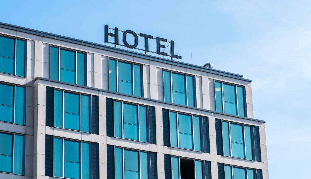 Modern hotel building with large blue-tinted windows and a bold 'HOTEL' sign on the rooftop against a clear blue sky