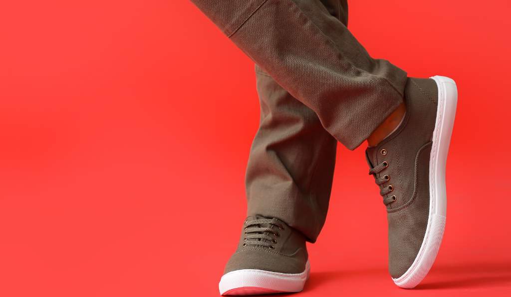 Stylish olive green canvas sneakers with white soles worn with matching pants against a bold red background