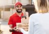 Hungry Howie’s $5, $10, $15 Deals A smiling delivery man in a red uniform and cap handing over pizza boxes and coffee cups to a customer wearing a white sweater outside a residential area food