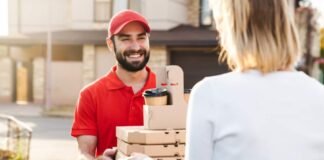 Hungry Howie’s $5, $10, $15 Deals A smiling delivery man in a red uniform and cap handing over pizza boxes and coffee cups to a customer wearing a white sweater outside a residential area food