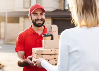 Hungry Howie’s $5, $10, $15 Deals A smiling delivery man in a red uniform and cap handing over pizza boxes and coffee cups to a customer wearing a white sweater outside a residential area food