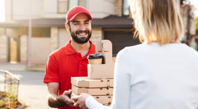 Hungry Howie’s $5, $10, $15 Deals A smiling delivery man in a red uniform and cap handing over pizza boxes and coffee cups to a customer wearing a white sweater outside a residential area food