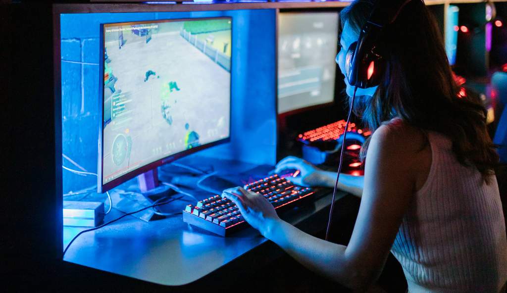 Young woman wearing a headset intensely playing a video game on a high-performance gaming PC in a dimly lit gaming setup with neon lighting