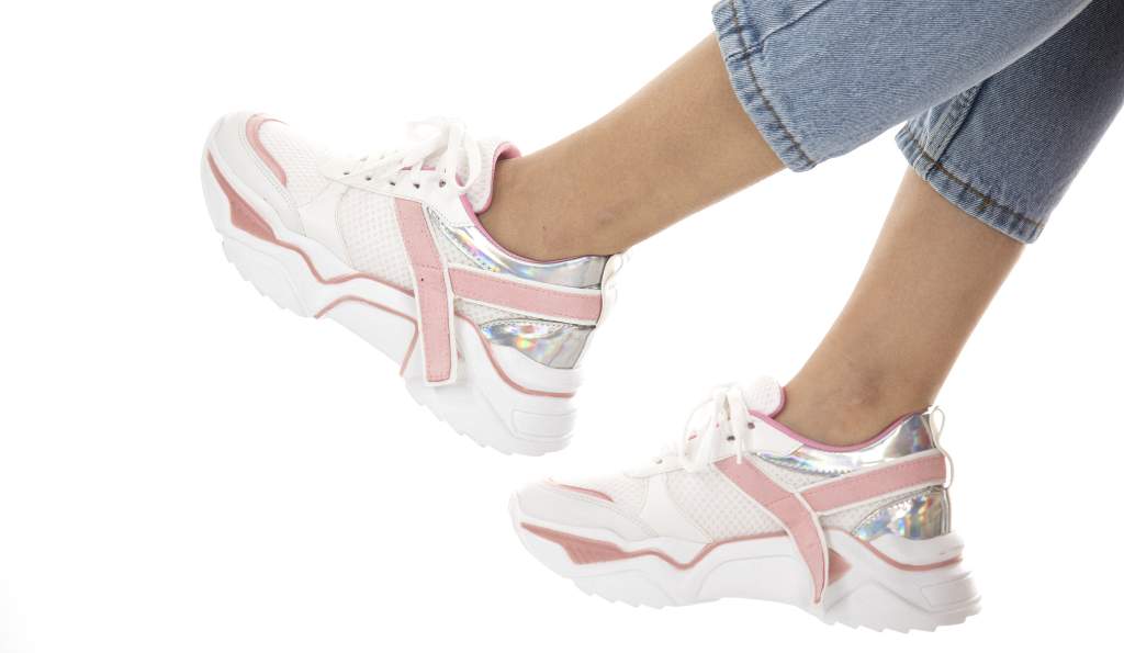 White and pink chunky sneakers with holographic details worn with cropped denim jeans against a white background shoes