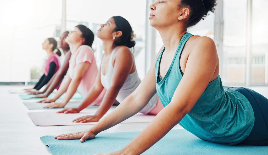 A group of women in a yoga class practicing the cobra pose on mats in a bright, modern studio with large windows wellness